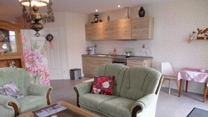 Ein Wohnzimmer mit zwei grünen Sesseln, einem Holztisch und einer Küche im Hintergrund.