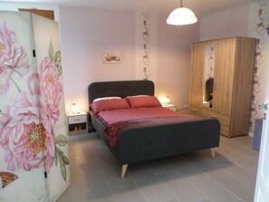 Quarto com cama, mesas de cabeceira, guarda-roupa e um ornamento floral na parede.
