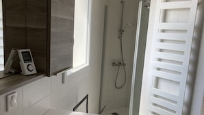Une salle de bain moderne avec une grande baignoire blanche, une douche dotée d’une porte en verre et un porte-serviettes blanc.