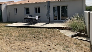 Une maison de plain-pied avec un toit en tuiles, une terrasse avec une table et des chaises, et un petit jardin.