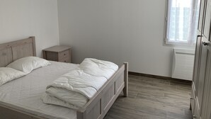 Une chambre avec un lit en bois, une table de chevet, un radiateur et une fenêtre avec des rideaux.