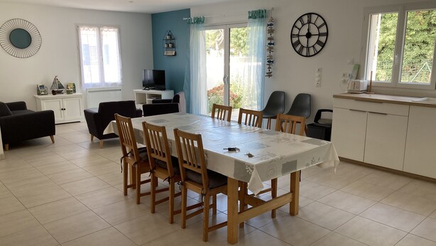 Un vaste espace de vie comprenant une table à manger, des chaises, un téléviseur et un coin cuisine avec une horloge.