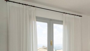 Quarto com cama, janela com cortinas e vista para edifícios.