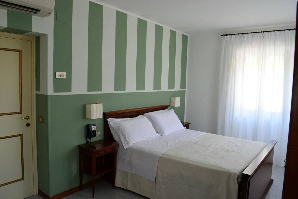 A hotel room with a bed, bedside tables, a telephone, and a window with curtains.