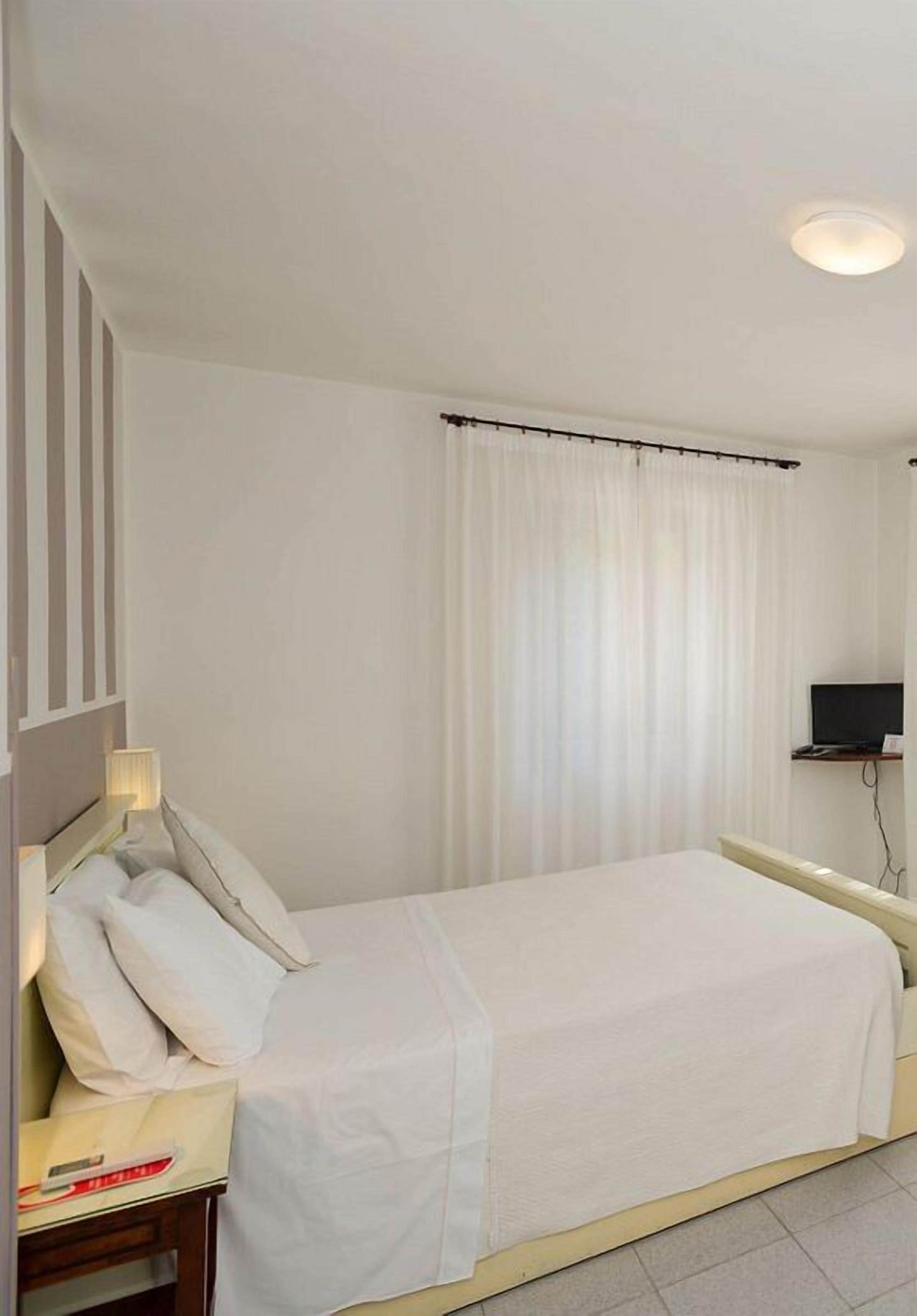 Una camera d'albergo con un letto, un comodino, una televisione e una finestra con tende.
