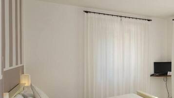 Una camera d'albergo con un letto, un comodino, una televisione e una finestra con tende.