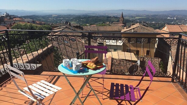 Terraço com mesa posta para o café da manhã, uma cadeira e vista para a cidade.