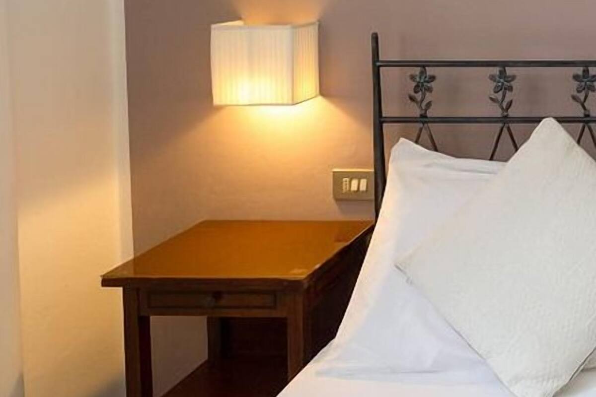 A hotel room with a bed, a nightstand, a lamp, and a wall with vertical stripes.