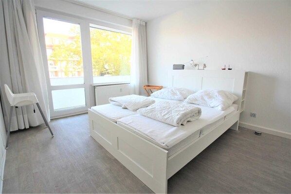 Une chambre moderne avec une grande fenêtre, un lit blanc et une petite chaise.