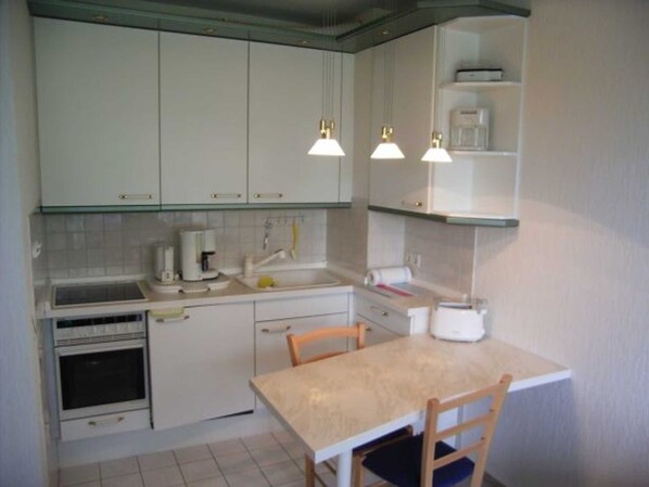 A compact kitchen with white cabinets, a coffee maker, a sink, and a small table with chairs.