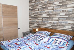 Un dormitorio con cama, cabecera de madera, mesita de noche con lámpara y pared con diseño de tablones de madera.