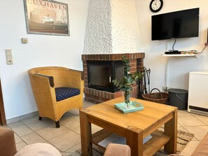 Uma sala de estar aconchegante com lareira de tijolos, móveis de vime, uma TV de tela plana e um pôster na parede.