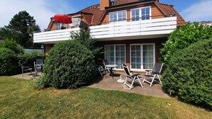 Une maison à deux étages dotée d’un balcon, d’une terrasse avec des meubles d’extérieur et d’une pelouse bien entretenue.