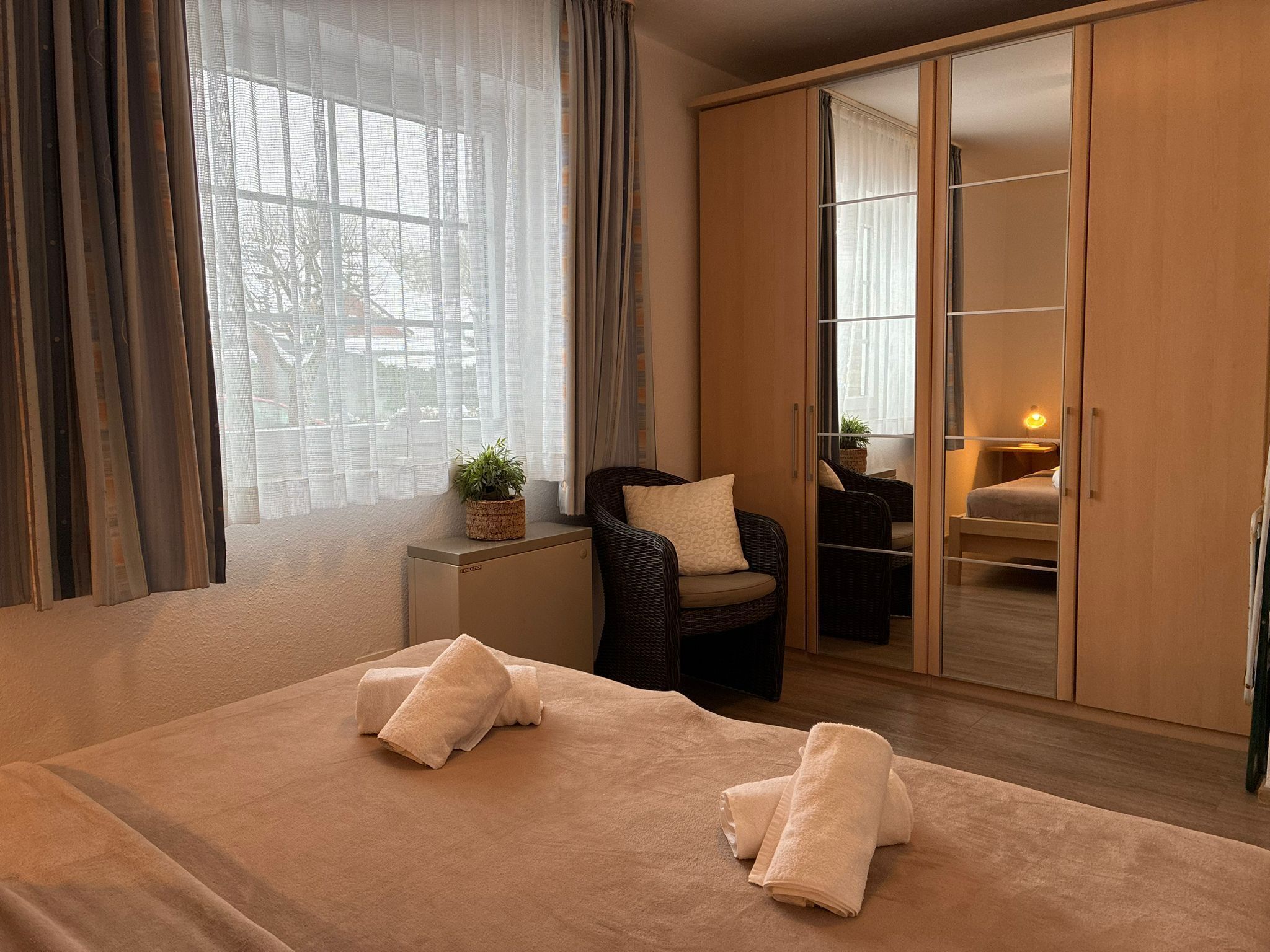 A bedroom with a large bed, two chairs, a wardrobe, and a window with curtains.
