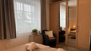 Ein Schlafzimmer mit einem großen Bett, zwei Stühlen, einem Kleiderschrank und einem Fenster mit Vorhängen.
