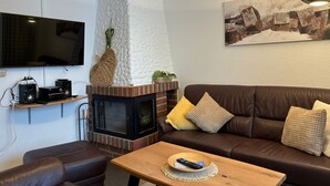 Ein gemütliches Wohnzimmer mit Kamin, einer braunen Ledersofa, einem Holztisch und einem an der Wand befestigten Fernseher.
