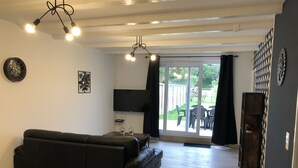 Ein modernes Wohnzimmer mit einem schwarzen Ledersofa, einem Flachbildfernseher und einer großen Schiebeglasdoor zum Außenbereich.