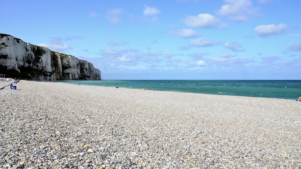 Ein Kiesstrand mit einer Klippe an einer Seite und dem Meer auf der anderen.