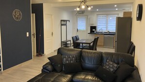 Ein modernes Wohnzimmer mit Ledersofa, einem Esstisch mit Stühlen und einer Küchenzeile inklusive Spüle und Schränken.
