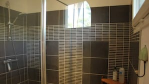 A shower area with a glass door, tiled walls, and a wooden shelf with toiletries. - Quiet house between ocean and Bassin d'Arcachon (Cap-Ferret)