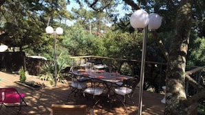 An outdoor deck with a round table and chairs, surrounded by trees and a wooden fence. - Quiet house between ocean and Bassin d'Arcachon (Cap-Ferret)