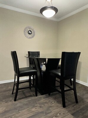 A dining area with a round table and four chairs, a wall clock, and a ceiling light fixture.