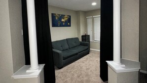 Een kamer met een grijs tapijt, een donkergrijze bank en een wereldkaart aan de muur.
