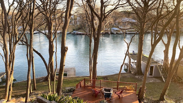 Un patio in legno con mobili da esterno, un braciere e vista su un lago con barche.