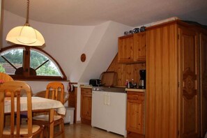 Cocina compacta con armarios de madera, una mesa de comedor con sillas y un ventanal con vistas a zonas verdes.