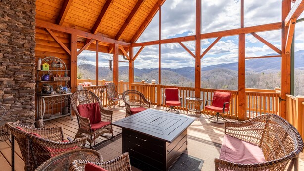 A wooden deck with wicker furniture and a stone wall, overlooking a mountainous landscape. - Beary Relaxing Cabin - Big views, two kitchens, hot tub, game table (Banner Elk)