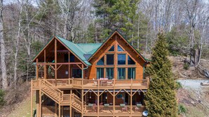 A two-story log cabin with a balcony and a deck, surrounded by trees. - Beary Relaxing Cabin - Big views, two kitchens, hot tub, game table (Banner Elk)