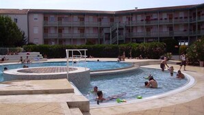 A swimming pool area with multiple pools, a diving board, and a building with balconies in the background.