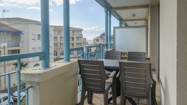 A balcony with a table and chairs, overlooking a street with buildings and parked cars.