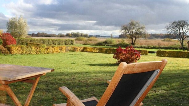 A garden with a wooden table and chairs, hedges, and trees.