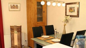 A dining area with a table set for four, surrounded by black chairs, a wooden cabinet with glass doors, and a vase with flowers.