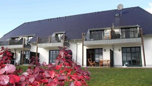 A modern two-story residential building with a dark roof, large windows, and balconies.