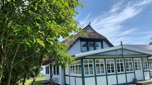 Ein traditionelles Haus mit Strohdach, einem Wintergarten mit weiß gefassten Fenstern und einem gepflegten Rasen.