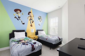 Une chambre avec deux lits, une fresque représentant des personnages de dessins animés, une fenêtre avec des stores et un bureau avec un ordinateur.