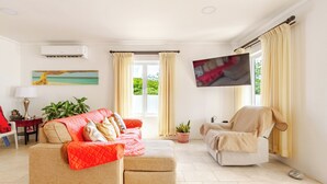 Een woonkamer met een beige bank, een rode bank, een aan de muur bevestigde televisie en een raam met gordijnen.