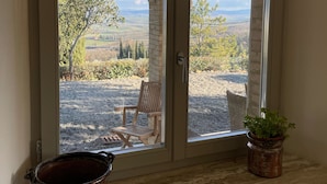 Una habitación con un amplio ventanal corredizo que da a un espacio exterior con una silla y una planta en maceta.