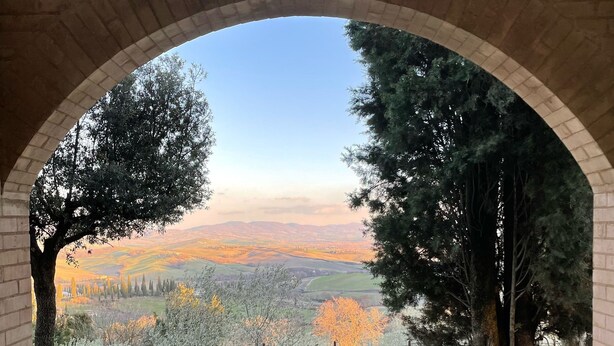 Vista a través de un arco que da a un paisaje rural con árboles y campos.