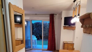 Una cocina compacta con mesa de madera y banco integrado, una puerta corrediza de vidrio que da a un patio, y un televisor montado sobre la puerta.