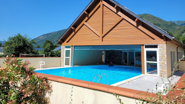 Una casa moderna con piscina, fachada de piedra y vistas a las montañas.