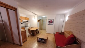 Un espacio habitable compacto con kitchenette, una zona de comedor y una sala de estar con un cojín rojo.