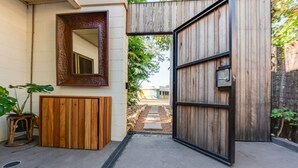 A modern entrance with a wooden door, a metal gate, and a concrete pathway leading to a garden area. - The Nightcliff Casinha | Boutique Coastal Retreat (Rapid Creek)