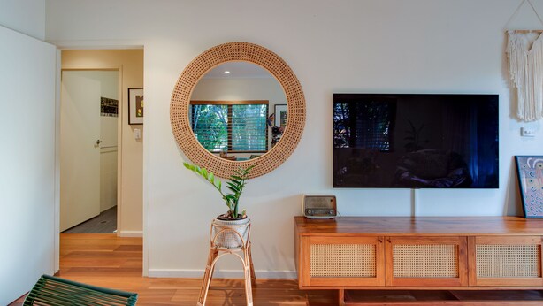 A living room with a large TV, a round mirror, and a wooden cabinet. - The Nightcliff Casinha | Boutique Coastal Retreat (Rapid Creek)