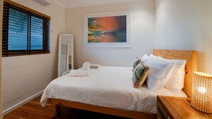 A neatly made bed with a white comforter, a wooden headboard, and a bedside lamp. - The Nightcliff Casinha | Boutique Coastal Retreat (Rapid Creek)
