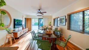 A spacious living room with a round glass table, green chairs, a ceiling fan, and a large TV. - The Nightcliff Casinha | Boutique Coastal Retreat (Rapid Creek)