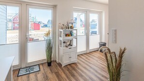 A room with large windows, a wooden floor, a white cabinet, and a view of a beach and buildings. - Gorgeous apartment in Büsum with sauna (Büsum)