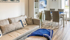 A living room with a beige sofa, a blue throw blanket, and a dining area with a white table and chairs. - Gorgeous apartment in Büsum with sauna (Büsum)